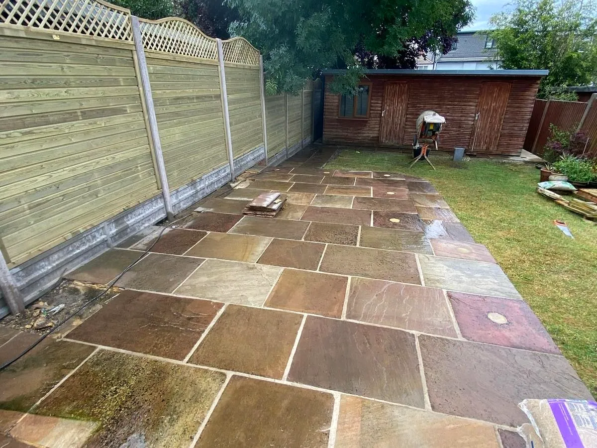 Autumn-toned riven Indian sandstone patio beside a close-board fence topped with a scalloped trellis