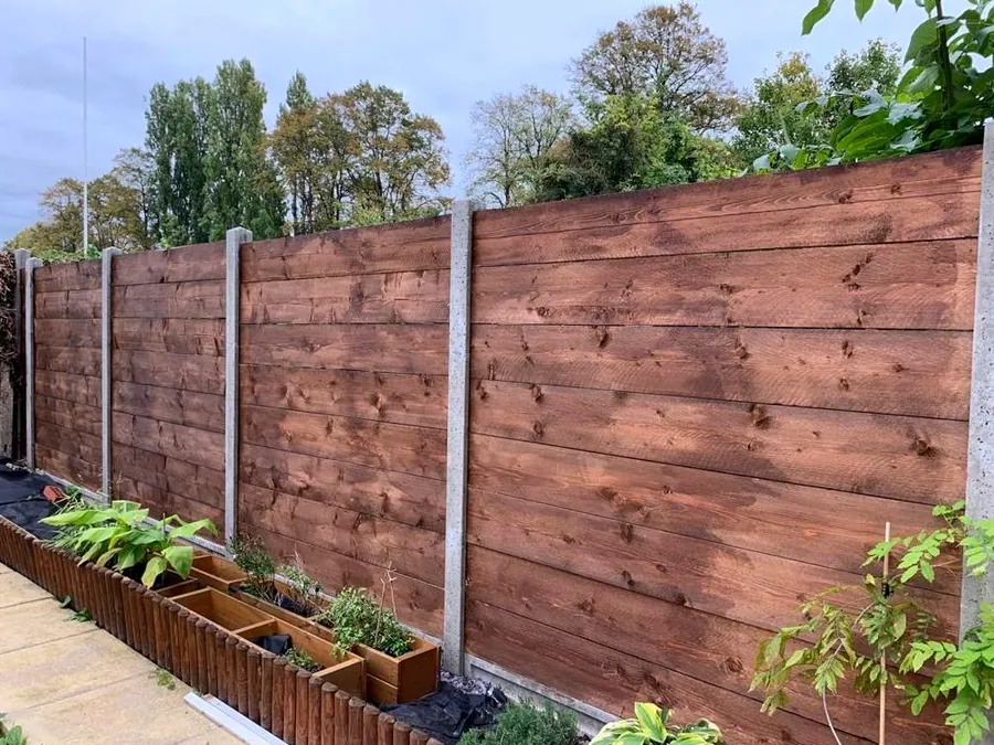 Horizontal stained feather-board fence on concrete posts with a low timber-log planter border