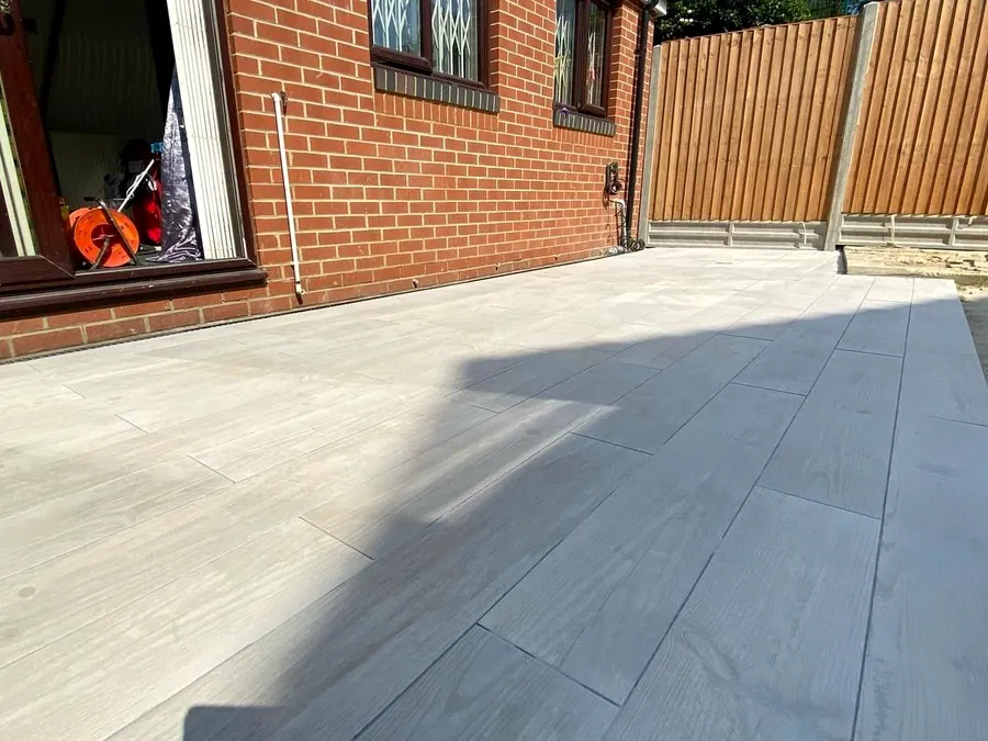 Grey wood-effect porcelain plank paving beside a red-brick house with feather-edge fencing