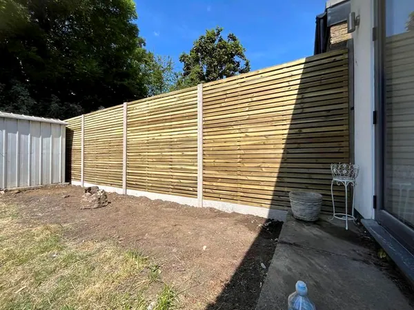 Contemporary horizontal slatted screen fence under a blue sky with a stone planter