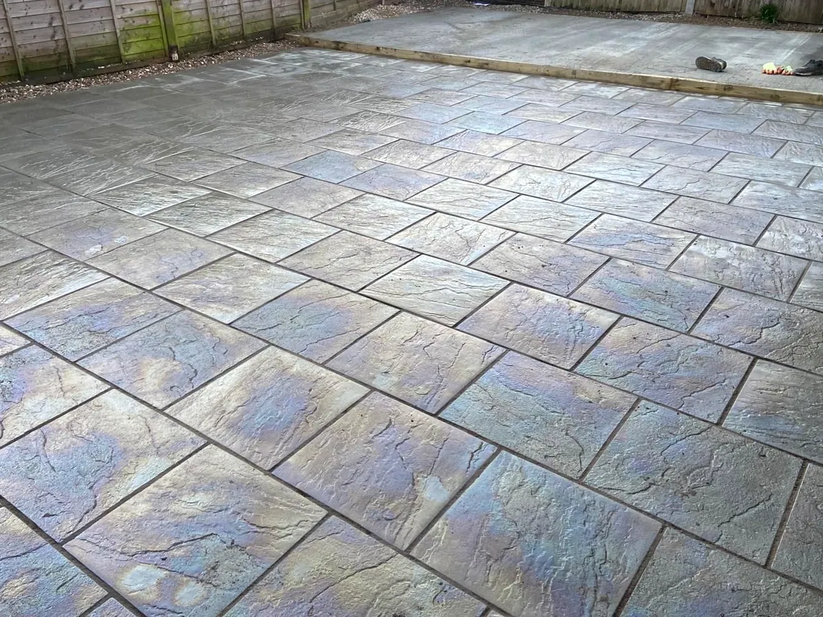 Grey pattern-imprinted riven paving patio with an overlap-panel fence behind