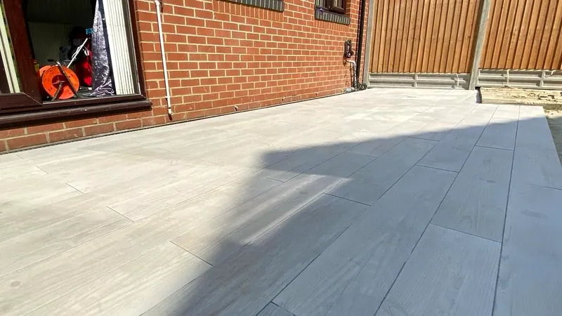 Grey wood-effect porcelain plank paving beside a red-brick house with feather-edge fencing