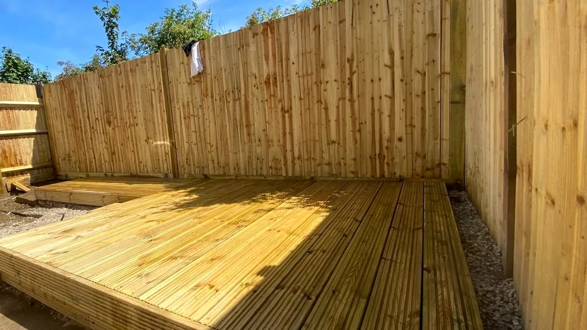 New softwood timber decking laid into a garden corner against feather-edge fencing under a clear sky