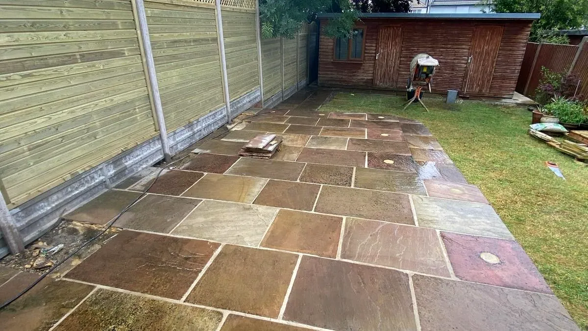 Autumn-toned riven Indian sandstone patio beside a close-board fence topped with a scalloped trellis