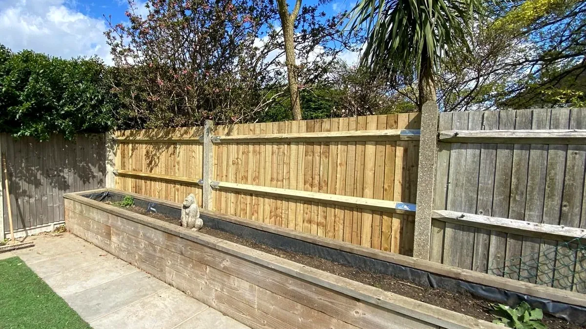 Timber sleeper raised bed with a paving strip and artificial lawn, a feather-edge fence and a cordyline palm