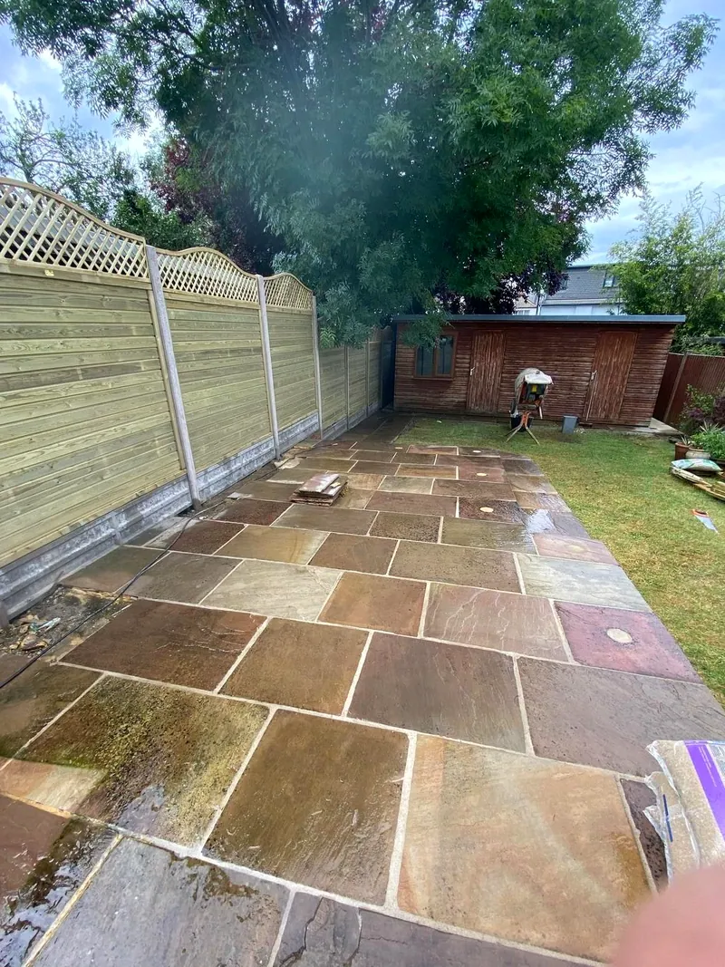Autumn-toned riven Indian sandstone patio beside a close-board fence topped with a scalloped trellis